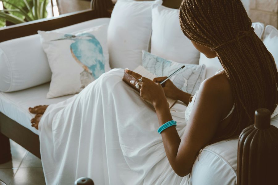 A Woman Sitting on Sofa while Writing in a Notebook